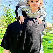Joyce joined the competition — help win amazing prizes! child, toddler, adult, piggyback, curly_hair, black_shirt, outdoor, park, grass, sunny, blue_sky, trees, smiling, playful, person, hand, footwear, casual_clothing, daytime, nature