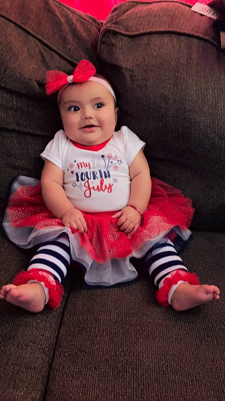 Isela is registered to the contest to win money with this photo: baby, baby_toddler_clothing, child, christmas, clothing, comfort, costume_hat, couch, dress, face, happy, headwear, joy, leg, pattern, person, pink, sitting, sleeve, smile