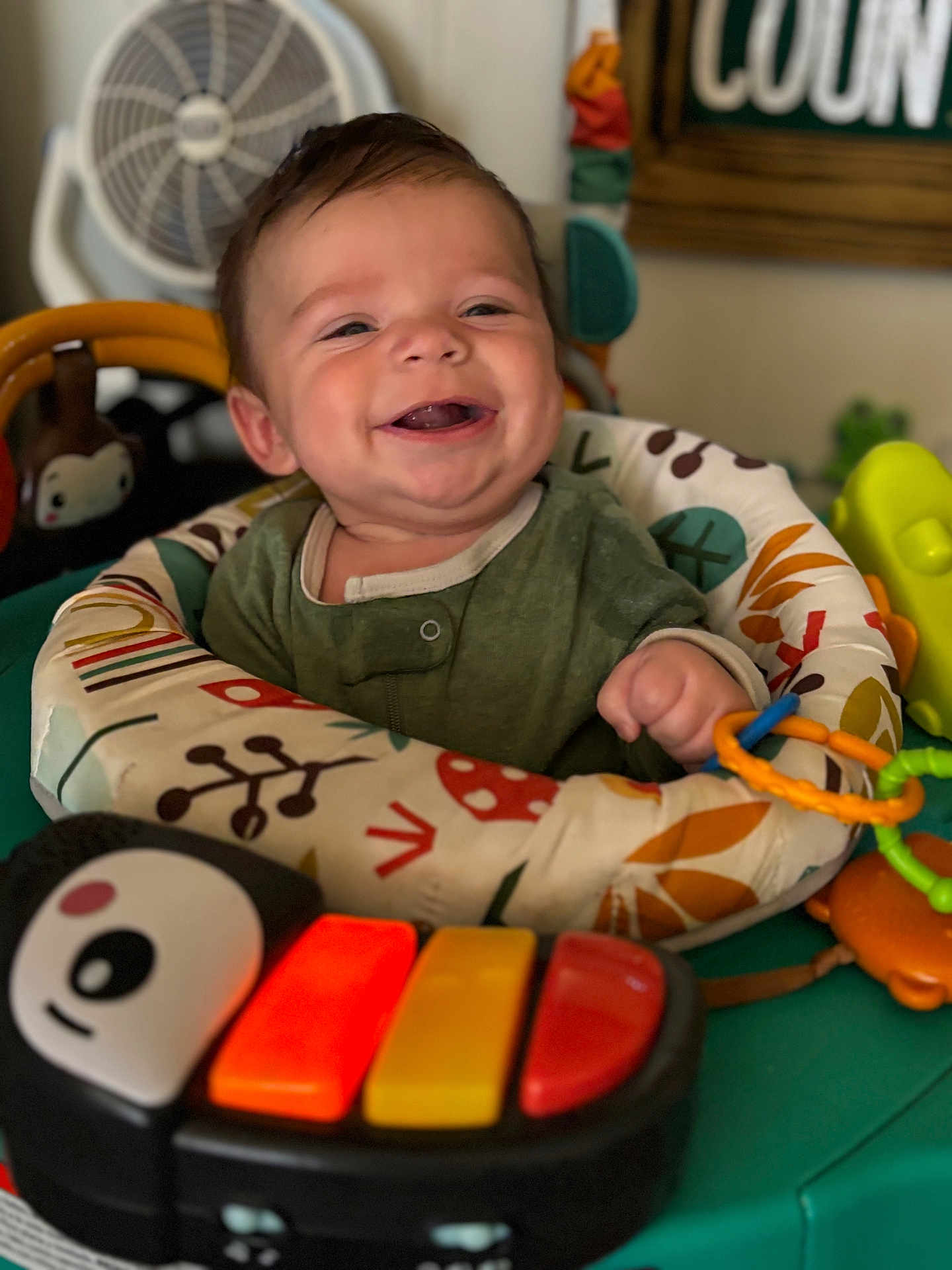 Hudson is registered to the contest to win money with this photo: baby, smiling, child, toy, activity_center, piano_toy, colorful, indoor, happy, face, hand, clothing, play, infant, furniture, fan, background, closeup, cute, person