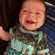 Hudson joined the competition — help win amazing prizes! baby, smiling, infant, face, clothing, tshirt, text, camo, blanket, lying_down, happy, child, portrait, cute, young, person, indoor, necklace, head, expression