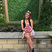 Sophia joined the competition — help win amazing prizes! woman, baby, smiling, outdoor, bench, greenery, plants, leafy_background, casual_clothing, sneakers, happy, portrait, nature, daylight, person, child, mother_and_child, sitting, family, cute