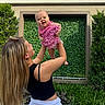 Sophia joined the competition — help win amazing prizes! baby, child, woman, outdoor, greenery, hedge, grass, smiling, happy, dress, pink, polka_dot, long_hair, black_top, white_skirt, holding, lifting, portrait, sunlight, nature