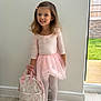 Aria is registered to the contest to win money with this photo: child, girl, ballet, tutu, pink, backpack, indoor, smile, hair_accessory, shoes, tights, floor, window, wall, wood_floor, natural_light, greenery, portrait, standing, cute