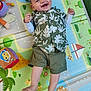 Elyam participe au concours pour gagner de l'argent avec cette photo : baby, smiling, play_mat, green_shirt, shorts, toy, colorful, happy, infant, child, indoors, cute, laughing, clothing, person, feet, hands, face, patterned_shirt, playtime