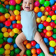 Elyam participe au concours pour gagner de l'argent avec cette photo : baby, child, smiling, happy, colorful, balls, ball_pit, play, fun, cute, infant, one_person, indoors, skin, face, legs, arms, bodysuit, joy, playful