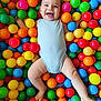 baby, child, smiling, happy, colorful, balls, ball_pit, play, fun, cute, infant, one_person, indoors, skin, face, legs, arms, bodysuit, joy, playful