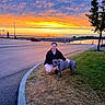 Frankie is registered to the contest to win money with this photo: car, clouds, curb, dog, evening, friendship, grass, landscape, leash, nature, outdoor, pavement, person, recreation, road, sky, smile, sunset, tree, water