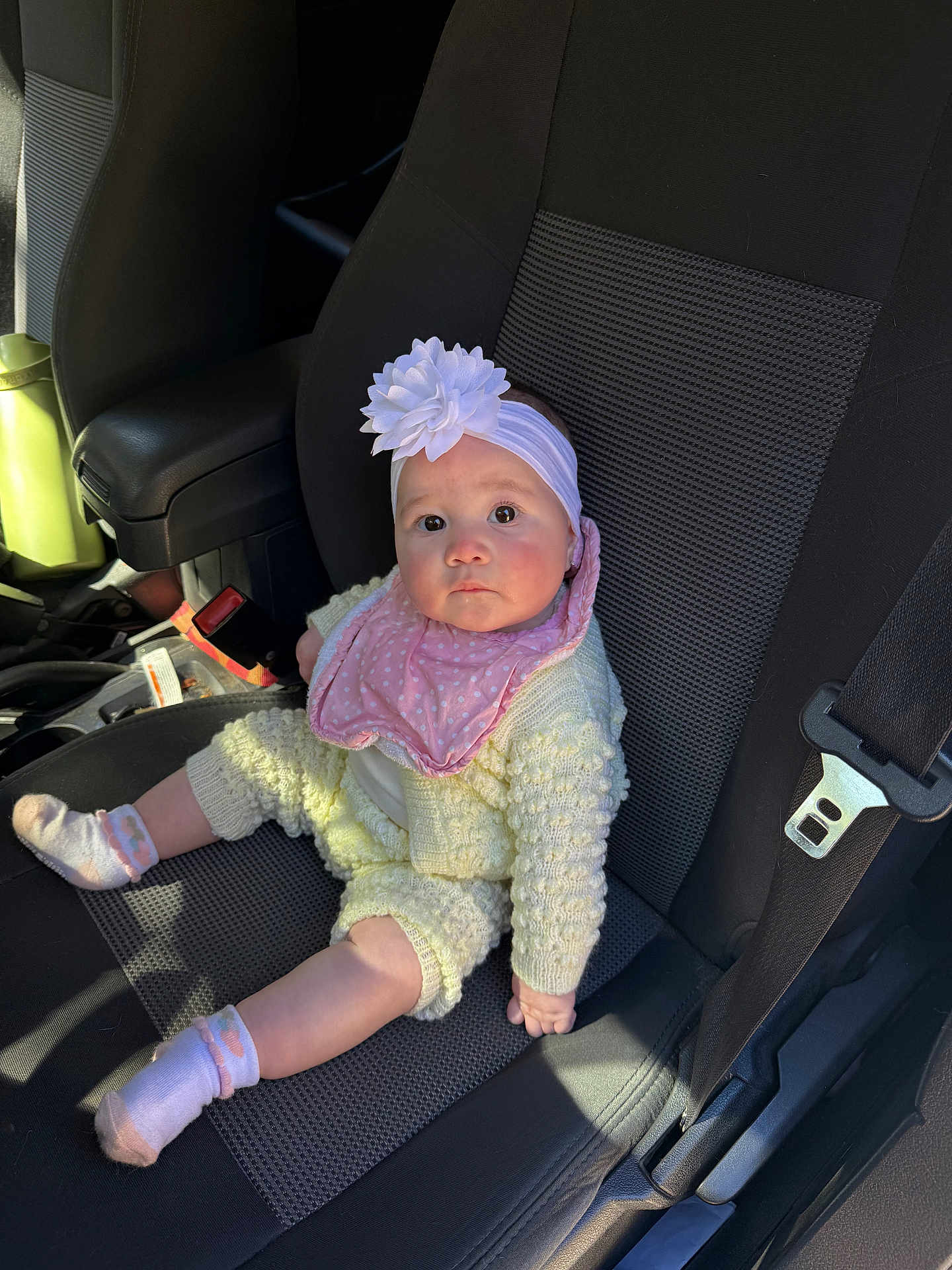Areya is registered to the contest to win money with this photo: baby, infant, child, flower_headband, headband, pink_bib, knit_outfit, socks, car_seat, car_interior, seat_belt, buckle, portrait, looking_up, big_eyes, cute, sitting, sunlight, hand, seat