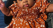 Kylie is registered to the contest to win money with this photo: baby, infant, child, dress, floral_pattern, hair_bow, cute, portrait, closeup, smiling, indoor, blanket, pillow, cozy, person, young_child, fashion, sitting, happy, skin