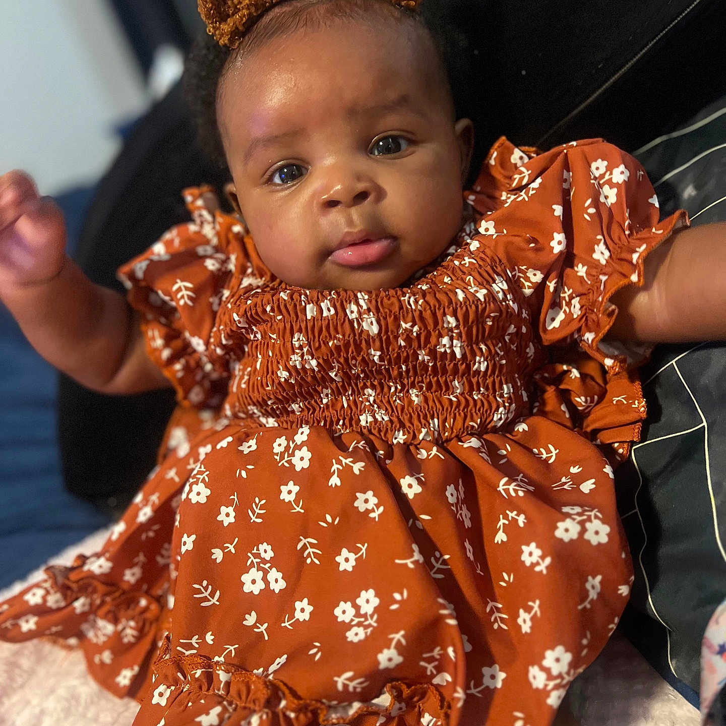 Kylie is registered to the contest to win money with this photo: baby, infant, child, dress, floral_pattern, hair_bow, cute, portrait, closeup, smiling, indoor, blanket, pillow, cozy, person, young_child, fashion, sitting, happy, skin