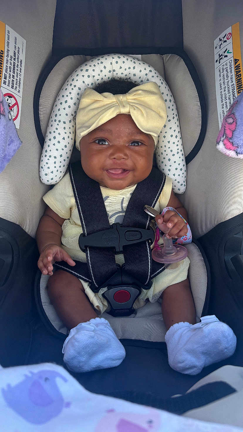 Myla joined the competition — help win amazing prizes! baby, child, car_seat, smiling, yellow_bow, pacifier, socks, infant, straps, cute, happy, clothing, seatbelt, headband, person, sitting, indoor, closeup, baby_accessory, toddler