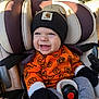 baby, child, car_seat, beanie, mittens, sweater, pumpkin_pattern, smile, happy, clothing, seatbelt, infant, cute, warm_clothing, autumn, indoor, person, headwear, portrait, cozy