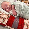 baby, infant, blanket, quilt, hospital, crib, nasal_tube, medical_tape, bed, sleeping, face, person, child, swaddled, soft_fabric, pattern, red, green, closeup, healthcare