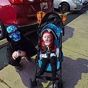 Kora is registered to the contest to win money with this photo: child, baby, costume, pirate, mask, skull, halloween, stroller, parking_lot, sidewalk, car, red_car, black_hoodie, outdoor, night, holiday, fun, kids, crouching, curious