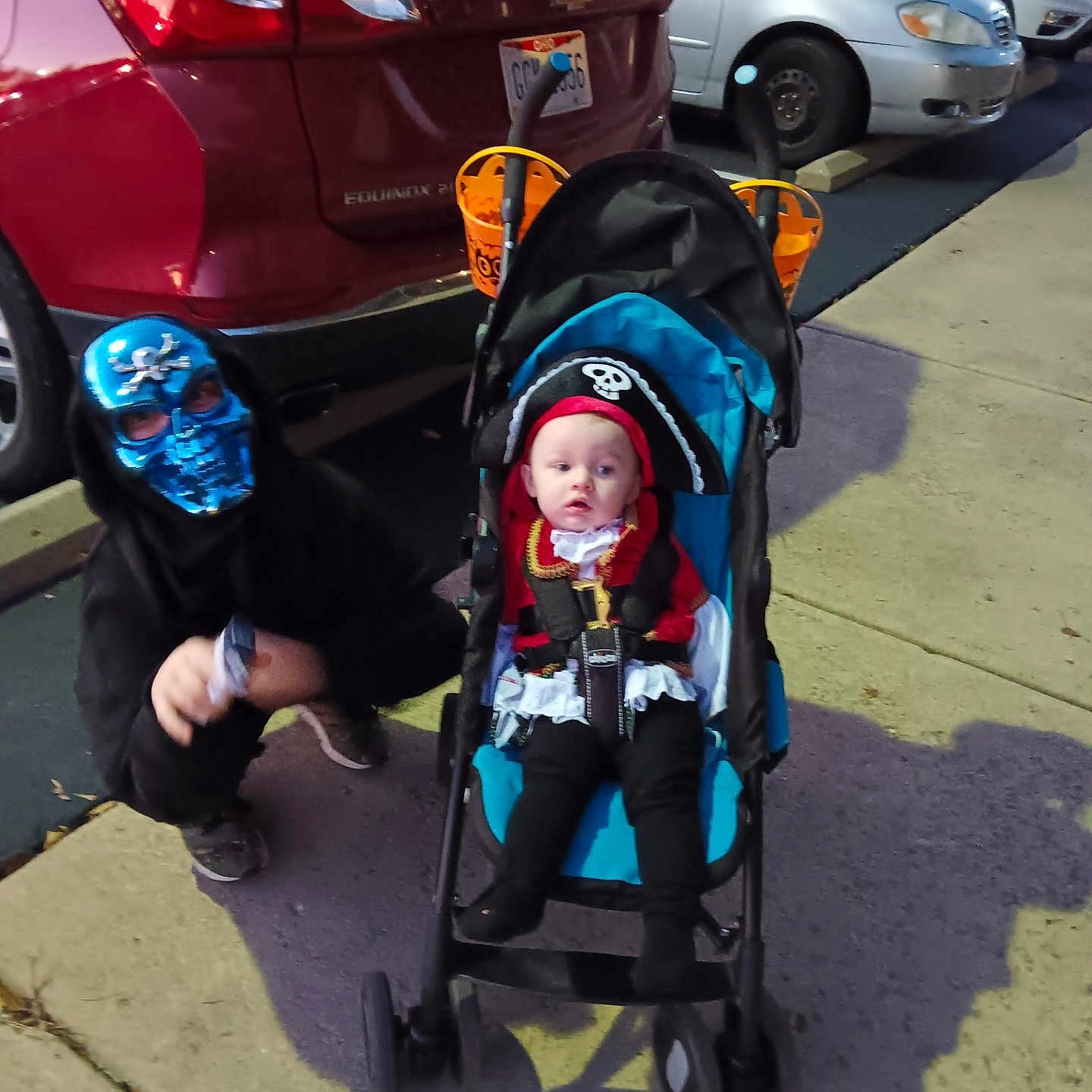 Kora is registered to the contest to win money with this photo: baby, black_hoodie, car, child, costume, crouching, curious, fun, halloween, holiday, kids, mask, night, outdoor, parking_lot, pirate, red_car, sidewalk, skull, stroller