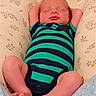 newborn, baby, infant, sleeping, portrait, striped_onesie, green_clothing, navy_clothing, floral_bedding, cushion, blanket, lying_down, arms_up, bare_feet, toes, closed_eyes, peaceful, indoors, closeup, child