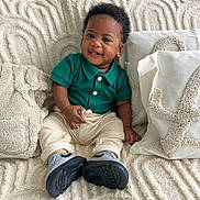 Kaïs a rejoint le concours — aidez-le/la à gagner de superbes lots ! baby, smiling, green_shirt, cream_pants, sneakers, couch, pillows, blanket, texture, happy, indoor, child, portrait, cute, cozy, seated, infant, clothing, furniture, home