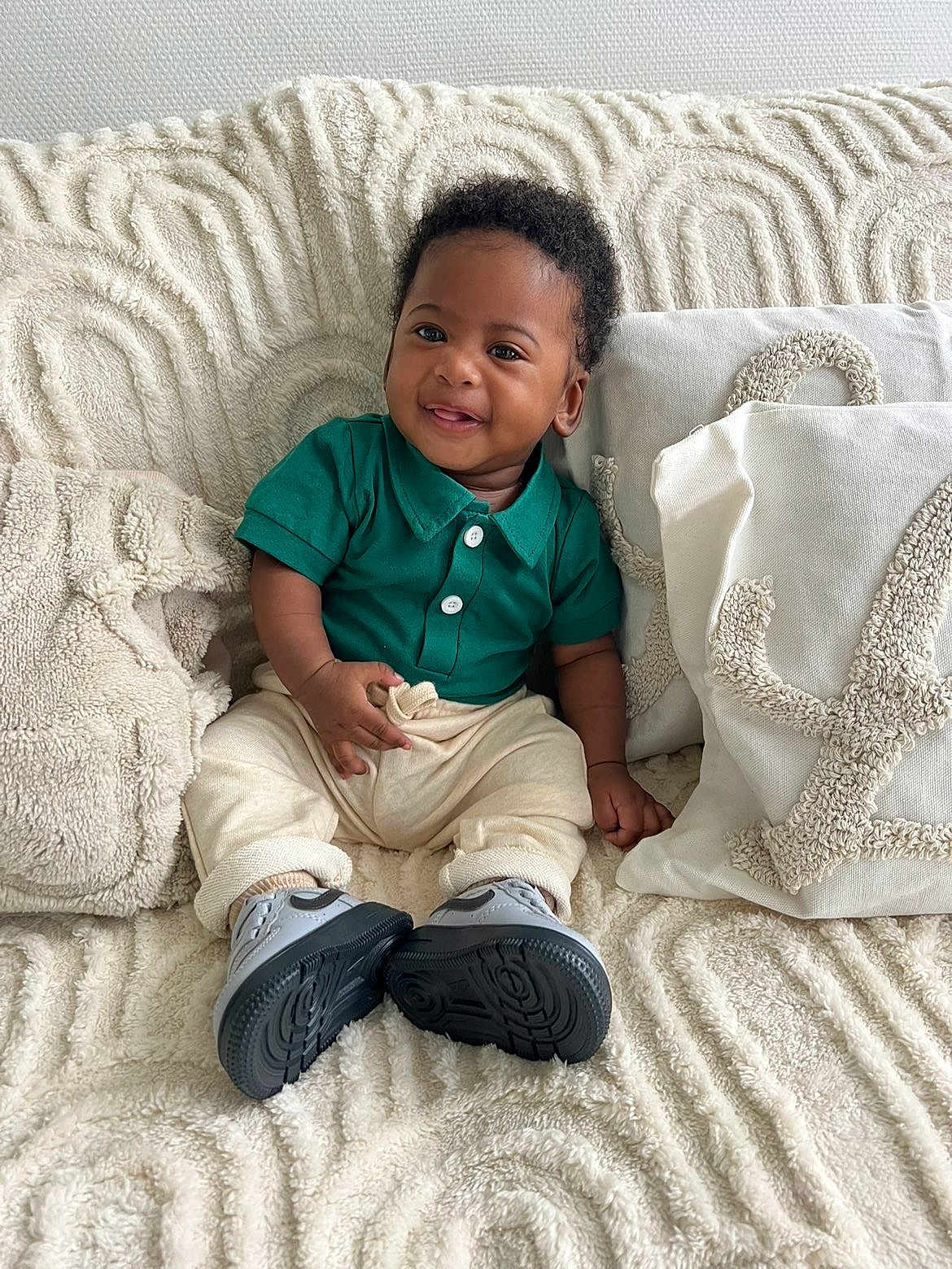 Kaïs a rejoint le concours — aidez-le/la à gagner de superbes lots ! baby, smiling, green_shirt, cream_pants, sneakers, couch, pillows, blanket, texture, happy, indoor, child, portrait, cute, cozy, seated, infant, clothing, furniture, home
