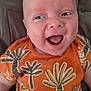 baby, child, smiling, orange_shirt, patterned_clothing, leaf_pattern, palm_tree_pattern, happy, face, head, blue_eyes, infant, cute, portrait, cushion, fabric, soft, indoor, person, closeup