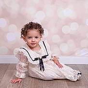 Ezalia is registered to the contest to win money with this photo: black_ribbon, bokeh_background, bracelet, child, curly_hair, cute, earrings, elegant, fashion, floor, indoor, jewelry, lace, necklace, portrait, sitting, smiling, toddler, white_dress, wooden_floor