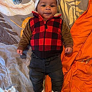 Nikko Lee is registered to the contest to win money with this photo: baby, child, infant, face, clothing, vest, hat, blanket, bedspread, pacifier, slippers, orange, pattern, lying_down, cute, portrait, indoor, smiling, warm_clothes, person