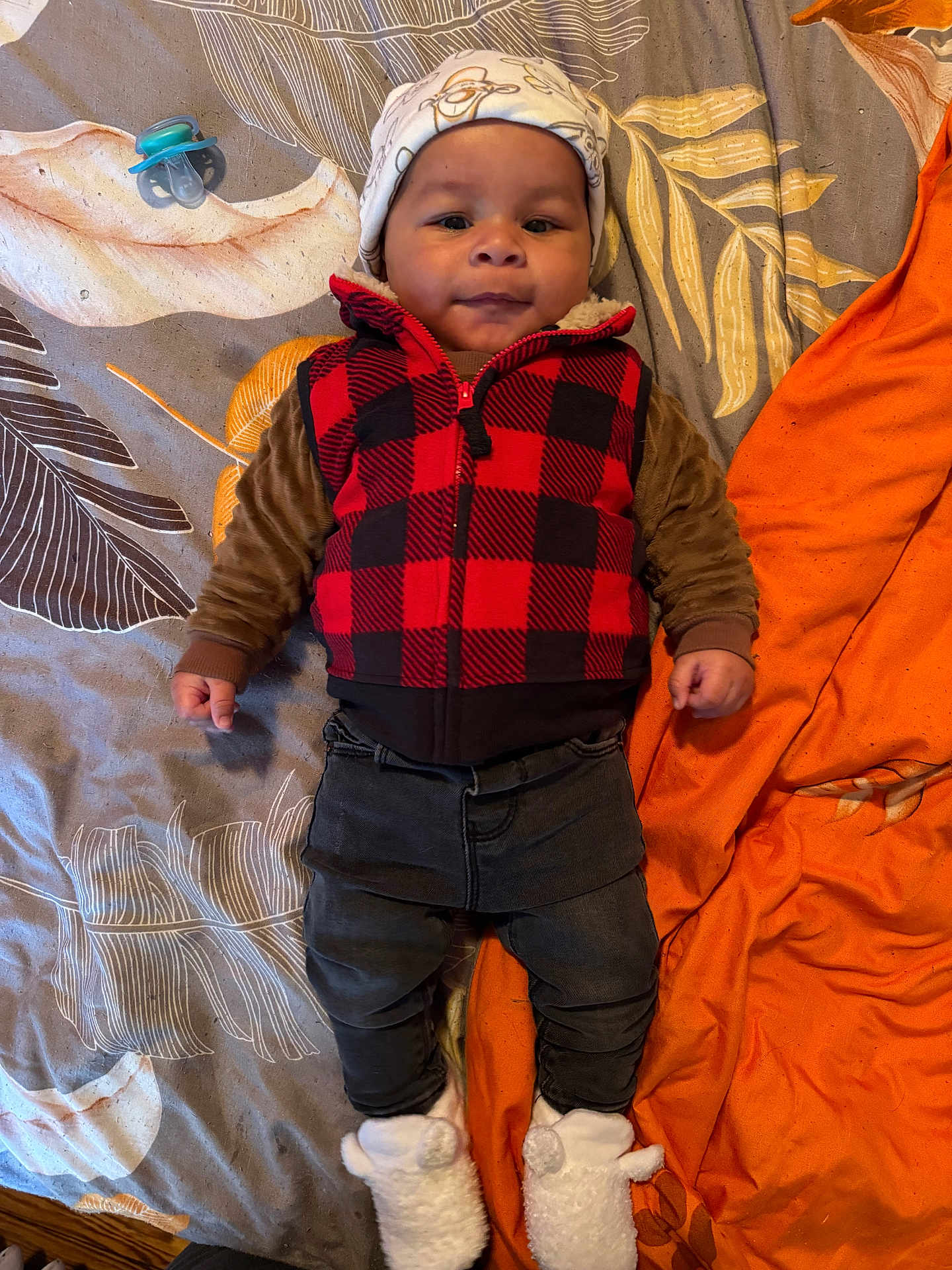 Nikko Lee is registered to the contest to win money with this photo: baby, child, infant, face, clothing, vest, hat, blanket, bedspread, pacifier, slippers, orange, pattern, lying_down, cute, portrait, indoor, smiling, warm_clothes, person