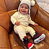 baby, brown, child, clothing, cozy, cute, footwear, happy, hat, indoor, infant, leather_chair, person, pom_poms, portrait, seated, shoes, smiling, sneakers, warm
