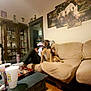Bailey is registered to the contest to win money with this photo: artwork, blanket, casual, clutter, coffee_table, couch, cup, decor, dog, furniture, glass_cabinet, home, indoor, living_room, person, relaxed, rhino_painting, shelving, sitting, wooden_floor