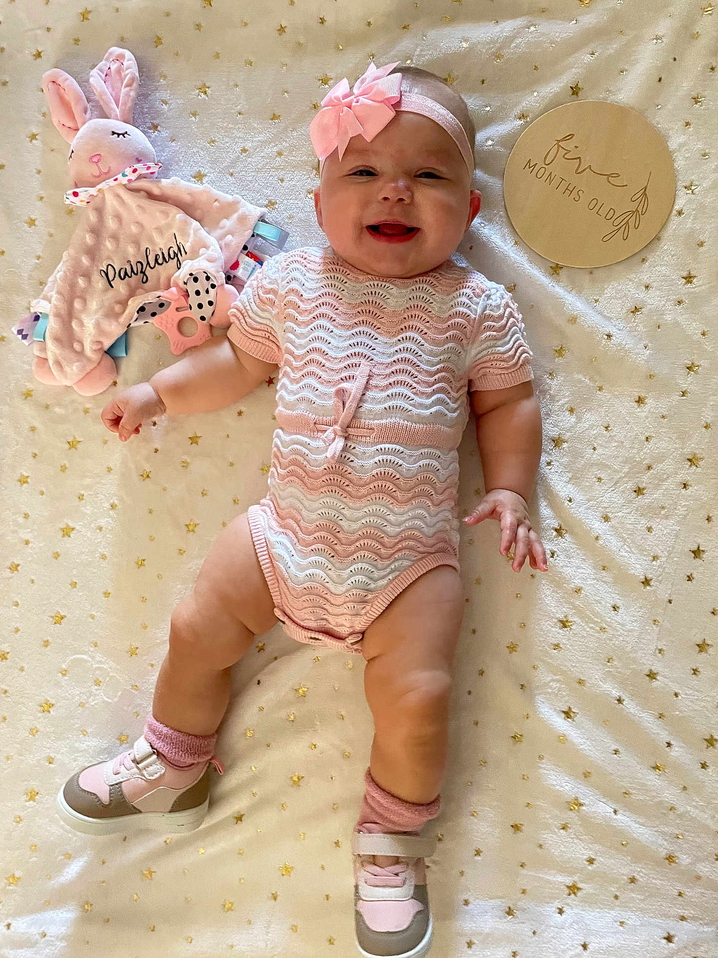 Paizleigh is registered to the contest to win money with this photo: baby, infant, girl, smile, headband, bow, knitted_clothing, socks, shoes, toy, stuffed_animal, blanket, star_pattern, plaque, wooden_sign, happy, lying_down, person, cute, indoor
