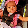 baby, infant, car_seat, headband, pink_clothing, baby_bottle, blanket, straps, safety, cute, child, portrait, close_up, indoors, seatbelt, expression, face, person, newborn, soft_toys