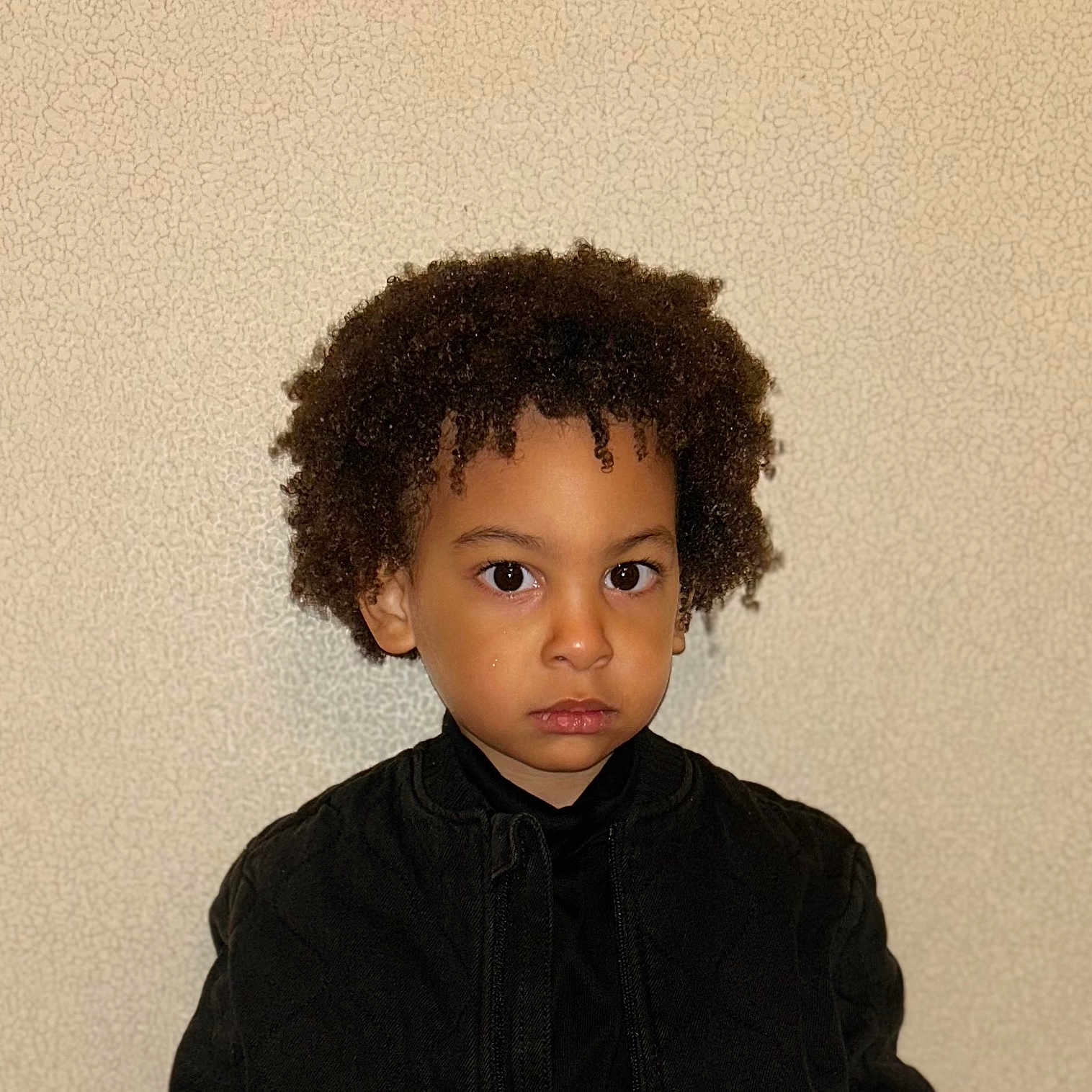 Idrissa Tshiananga participe au concours pour gagner de l'argent avec cette photo : black_jacket, boy, brown_eyes, casual_clothing, child, curly_hair, eyebrows, face, hairstyle, indoor, lips, looking_at_camera, neutral_background, nostrils, person, portrait, serious_expression, skin_tone, standing, young