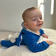 Ari a rejoint le concours — aidez-le/la à gagner de superbes lots ! baby, infant, smiling, blue_onesie, hoodie, tummy_time, blanket, white_bedding, bed, portrait, close_up, cute, hand, face, soft_light, indoor, bokeh, skin, cheeks, happy