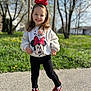 child, girl, toddler, smile, headband, bow, minnie_mouse, sweatshirt, cartoon, outdoors, grass, trees, sneakers, red_shoes, standing, portrait, happy, sunlight, spring, sidewalk