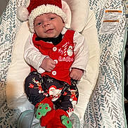 Sebastian is registered to the contest to win money with this photo: baby, infant, christmas, holiday_clothing, santa_hat, red_vest, black_bowtie, patterned_pants, christmas_socks, baby_seat, fabric_pattern, smiling, face, hands, feet, indoor, cute, festive, portrait, cozy