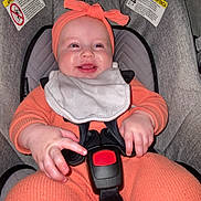 Oaklynn is registered to the contest to win money with this photo: baby, bib, car_seat, child, chubby_hands, closeup, comfortable, cute, happiness, headband, headwear, indoors, infant, joy, orange_clothing, person, safety_harness, seat, sitting, smile