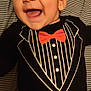 baby, child, smiling, laughing, tuxedo_onesie, red_bow_tie, striped_bedding, checkered_blanket, happy, portrait, indoor, clothing, cute, infant, face, head, person, baby_wear, playful, joyful