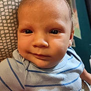 Gavin is registered to the contest to win money with this photo: baby, infant, face, person, blue_clothing, striped_clothing, onesie, smile, eyes, hand, holding, indoor, portrait, closeup, head, skin, cute, child, human, newborn