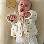 baby, infant, two_months, milestone_sign, wooden_disc, blanket, lying_down, tongue_out, cute, jacket, cherry_pattern, ribbed_pants, hands, portrait, close_up, milestone_photo, soft_texture, infant_clothing, bedding, newborn