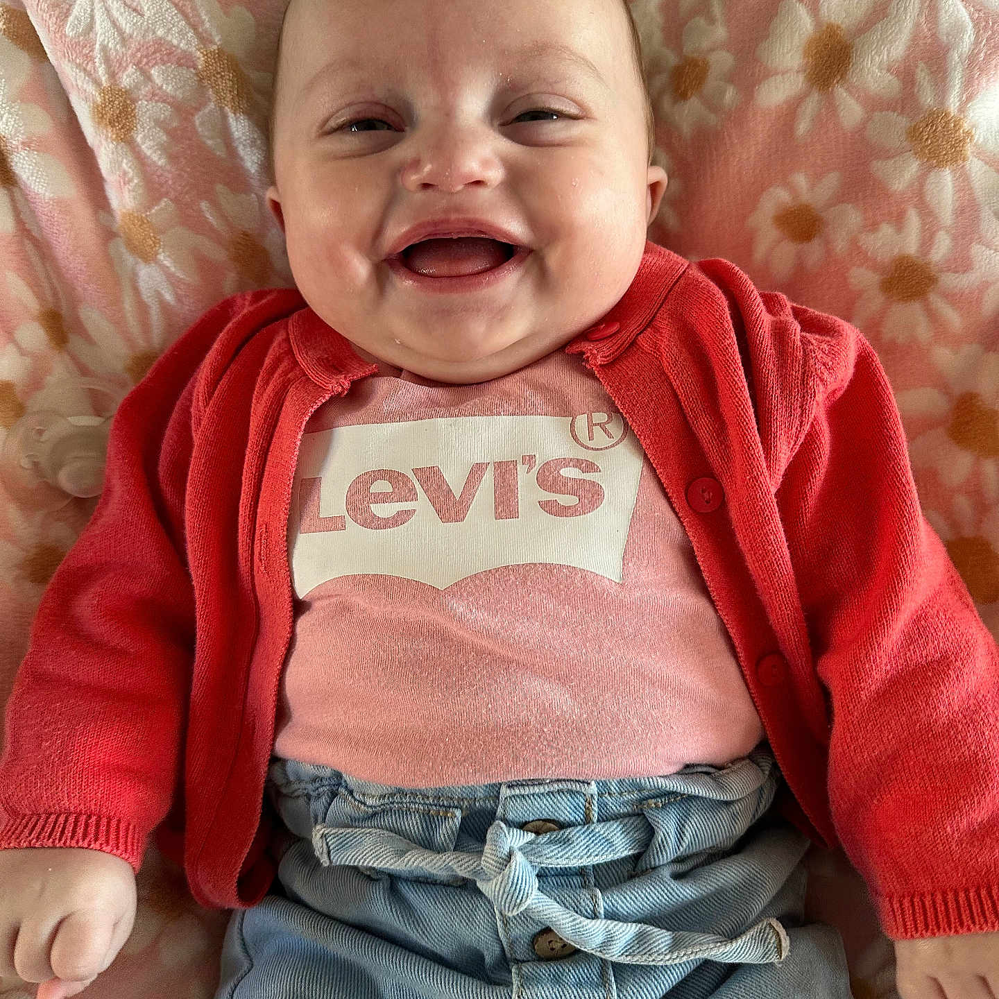 Zélya participe au concours pour gagner de l'argent avec cette photo : baby, blanket, cardigan, chubby_cheeks, cute, denim, face, floral_blanket, hands, happy, indoor, infant, jeans, levis_logo, lying_down, onesie, pacifier, pink, portrait, smiling