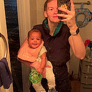 Jahmai is registered to the contest to win money with this photo: baby, person, mirror, bathroom, selfie, smile, toy, bib, towel, phone, watch, tiles, door, clothing, drawer, child, holding, green_ball, reflection, casual