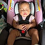 baby, car_seat, sleeping, infant, pink, black, sandals, hands_folded, toy, blanket, child, indoors, peaceful, cute, young, resting, seatbelt, clothing, footwear, portrait