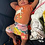 baby, child, infant, unicorn, orange_shirt, floral_shorts, pacifier, blankets, couch, relaxed, smiling, clothing, indoors, person, cute, happy, lying_down, tattoo, colorful, comfort