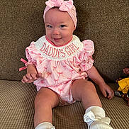 Laylani is registered to the contest to win money with this photo: baby, girl, pink_outfit, headband, bow, smiling, couch, infant, cute, child, sitting, white_shoes, indoors, happy, portrait, small_baby, soft_lighting, comfortable, clothing, baby_accessory