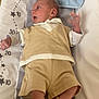 baby, infant, child, changing_mat, clothing, beige, shorts, vest, towel, floor, wooden_floor, sneakers, footwear, person, indoor, measurement, stars, padded_surface, looking_sideways, casual
