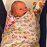 baby, infant, child, swaddled, blanket, floral_pattern, plush_toy, giraffe, nursery, chair, seated, portrait, face, eyes, awake, indoors, cozy, pink, colorful, photography