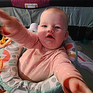 Raven is registered to the contest to win money with this photo: baby, infant, child, reaching, arm, hand, face, eyes, open_mouth, cheeks, bouncer, seat, toy, onesie, patterned_fabric, crib, nursery, indoor, portrait, playtime