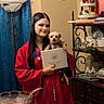 person, dog, graduation_gown, diploma, indoor, lamp, curtain, shelf, decor, vintage, table, glass_bowl, food, ceramic, smile, long_hair, black_hair, small_dog, medal, home