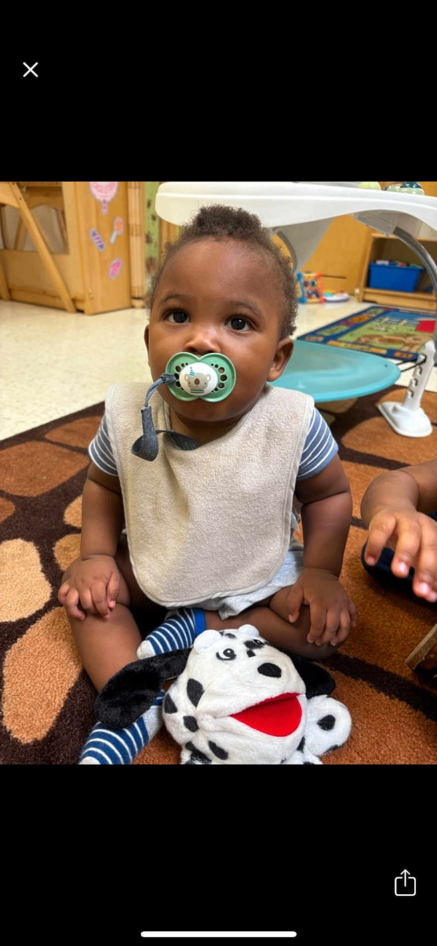 Kingston is registered to the contest to win money with this photo: toddler, pacifier, plush_toy, carpet, indoor, child, sitting, bib, striped_clothing, hand, toy, classroom, furniture, floor, play, cute, baby, expression, young_child, person