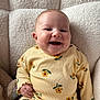 armchair, baby, casual_clothing, child, comfort, cozy, cute, expression, floral_pattern, happy, indoors, infant, person, portrait, seated, smiling, soft_texture, warm_lighting, yellow_outfit, young_child