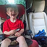 Ryder is registered to the contest to win money with this photo: child, car_seat, red_shirt, laughing, vehicle_interior, seatbelt, blue_sneakers, car_window, greenery, beige_seat, happy, young_child, sitting, casual_clothing, interior, daylight, smile, kid, seat, car